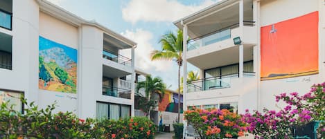 Un hotel con un paseo central bordeado por edificios con balcones, una palmera y flores coloridas.