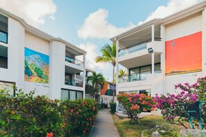 A hotel with a central walkway flanked by buildings with balconies, a palm tree, and colorful flowers. - Hommage Hotel & Residences (Nettle Bay)