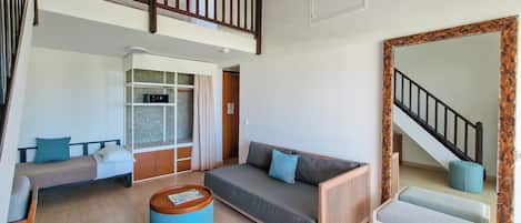 Amplia sala de estar con techo alto, una escalera, un conjunto de sofás, una mesa de centro y un espejo grande.