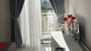 A modern room with a balcony, grey curtains, a white desk, a red vase with flowers, and a white chair. - Chiaia Guest House (Naples)