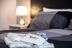 A neatly made bed with a pillow, a bedside lamp, and a set of towels with the logo "bri Bed & Breakfast". - Brio Bed & Breakfast (Agrigento)