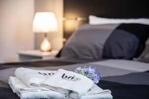 Una cama bien hecha con una almohada, una lámpara de noche y un juego de toallas con el logotipo 