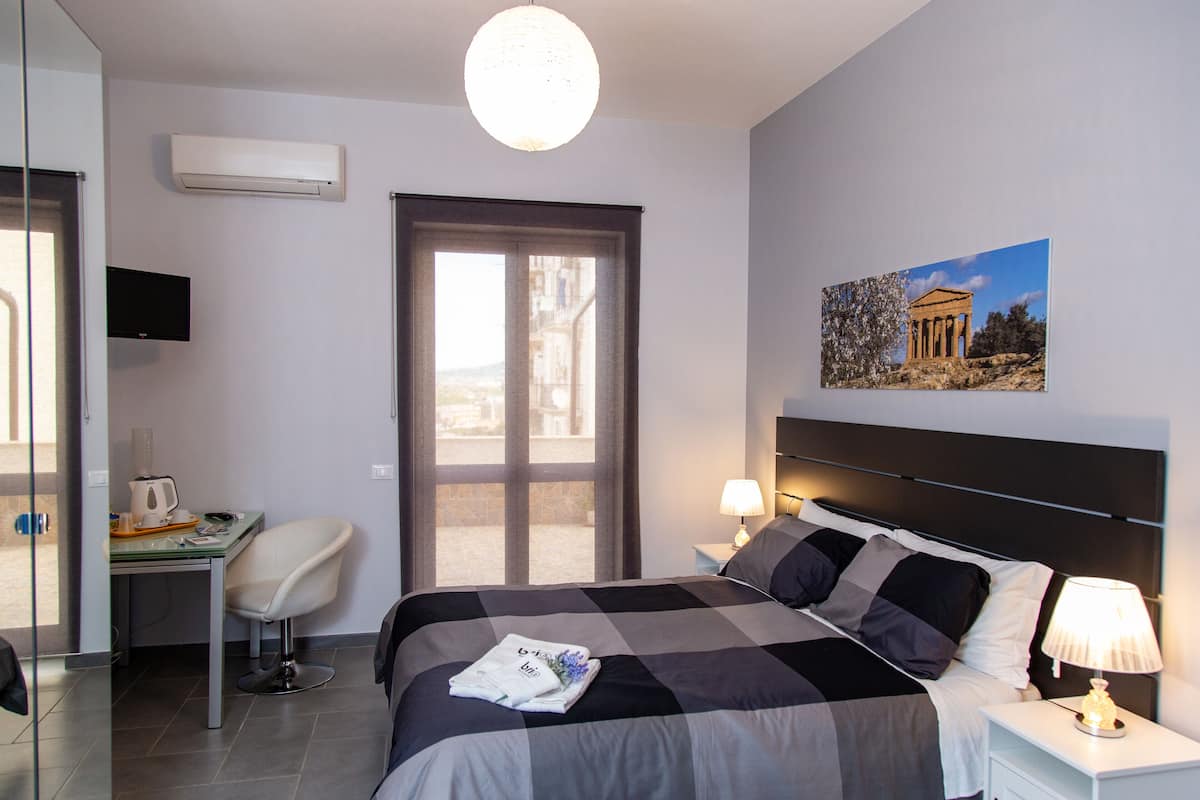 Una habitación de hotel con una cama, un escritorio, una silla, un televisor, una ventana y un cuadro en la pared.