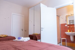 Habitación de hotel con cama, armario, baño con lavabo y espejo, y un taburete pequeño.