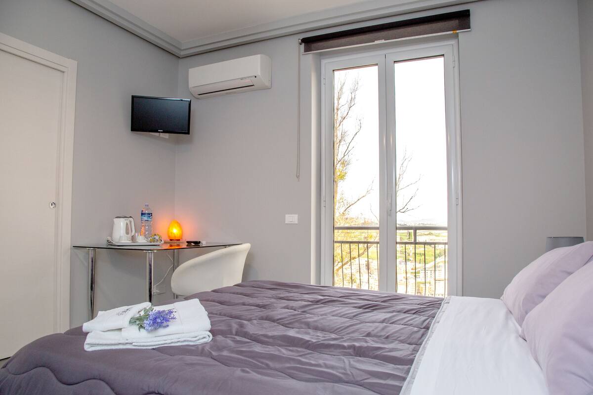 Habitación de hotel con cama, escritorio y silla, televisor y ventana con vista al exterior.