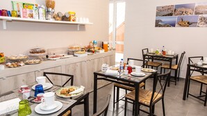 A breakfast buffet with various food items and beverages, multiple tables and chairs, and a wall with pictures. - Brio Bed & Breakfast (Agrigento)