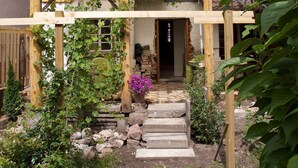 Een houten huis met een pannendak, een houten pergola en een stenen trap naar de ingang.