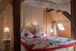 A cozy bedroom with a canopy bed, floral bedding, and a small bedside table with a lamp. - Historisches Gerberhaus (Alpirsbach)