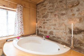 A bathroom with a stone wall, a wooden window with a floral curtain, and a bathtub with candles. - Historisches Gerberhaus (Alpirsbach)
