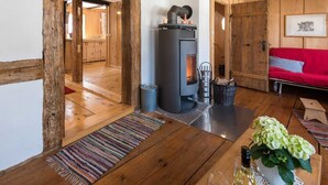 Een gezellige kamer met houten inrichting, een centraal gelegen openhaard, een rode bank en een eettafel met een bloemenvaas.