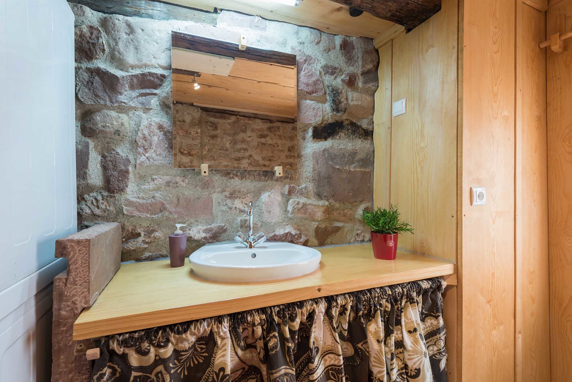 A bathroom with a stone wall, wooden countertop, and a sink.