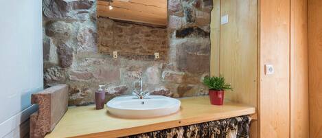 A bathroom with a stone wall, wooden countertop, and a sink.