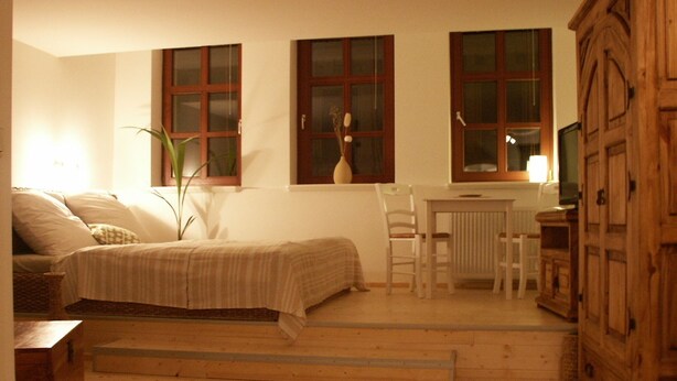 Een gezellige kamer met een bed, een bureau en een stoel. Drie ramen en een kastje zijn aanwezig.