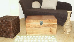 Een houten kist met een metalen sluiting, een geweven mand, een geweven vaas, en een vloerkleed met patroon op een houten vloer.
