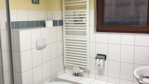 Een badkamer met een toilet, een wastafel, een handdoekrek, een raam en een douche.