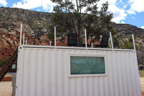 A white metal building with a window and a metal railing on top. - Mini Farmhouse Style Container Home #2 (Orderville)