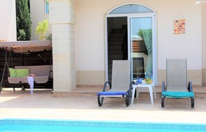 Un área junto a la piscina con sillones de descanso, un espacio de estar cubierto y una escalera que lleva a un nivel superior.