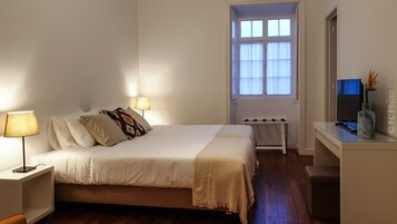 Un dormitorio ordenado con cama, lámparas de noche, una mesita y un ventanal con cortinas.