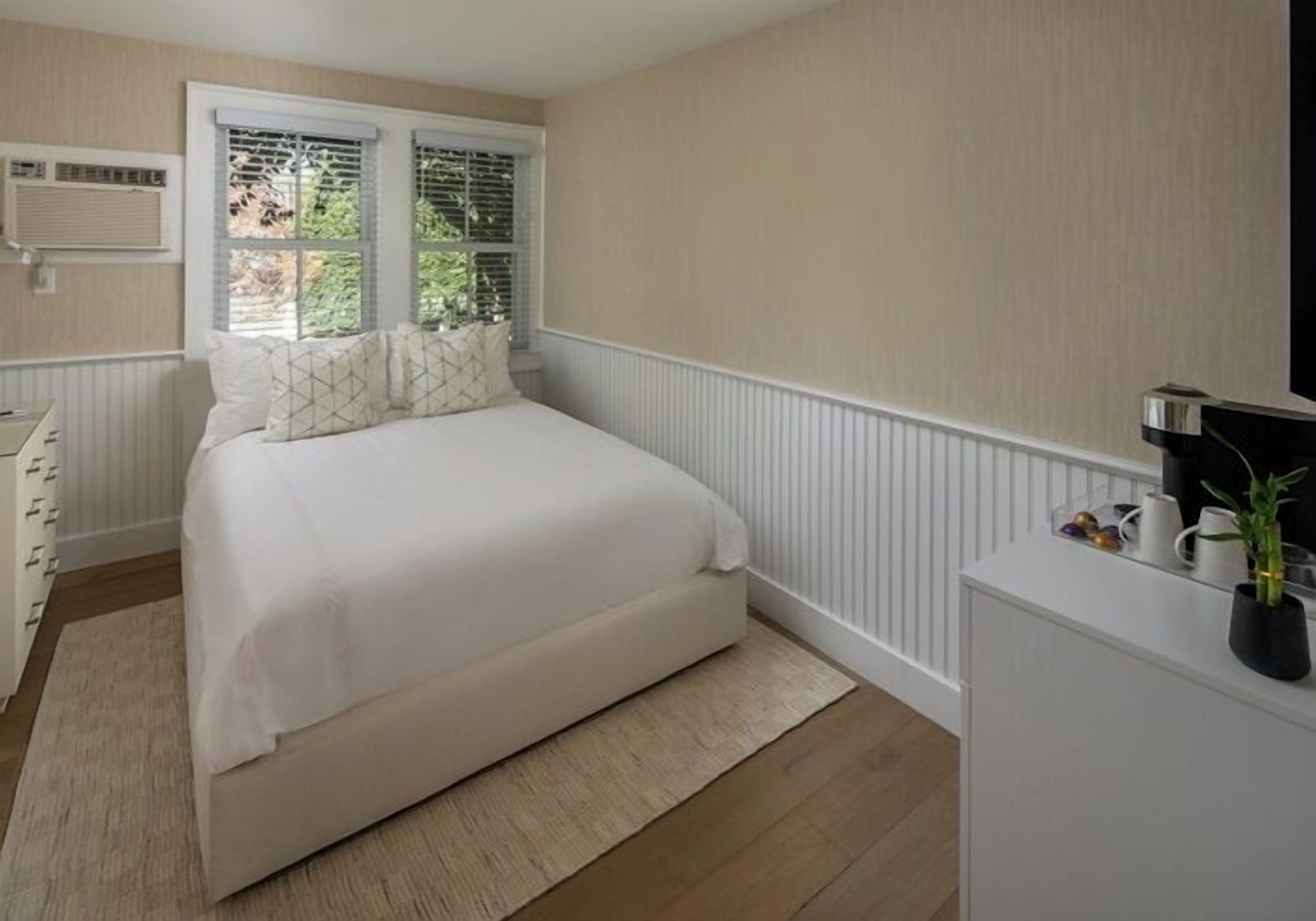 Un dormitorio con cama, cómoda, radiador y ventana con persianas.