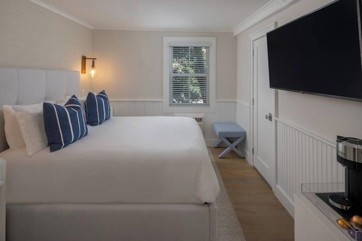 A bedroom with a bed, pillows, a window, a television, and a coffee machine.