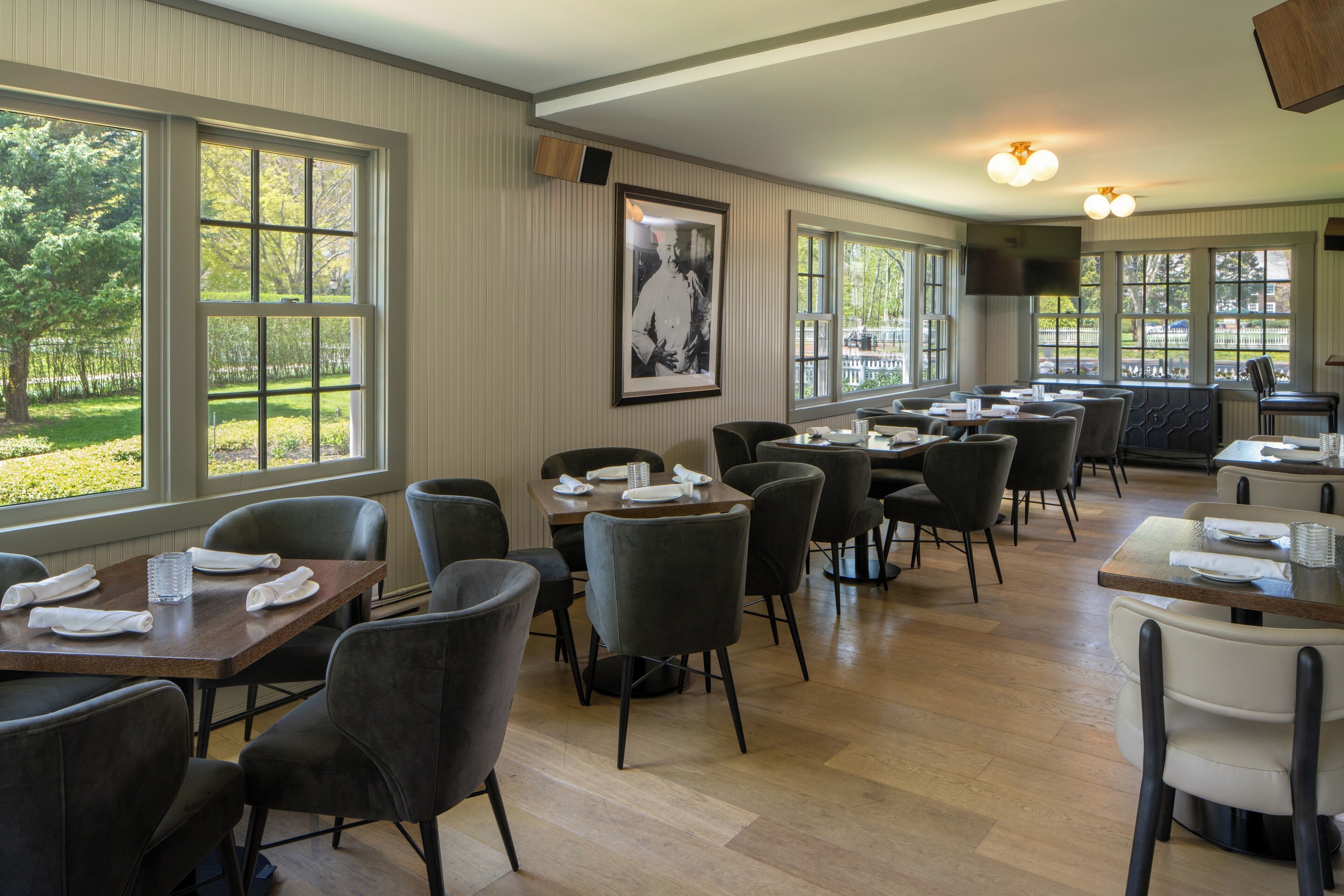 A restaurant with multiple tables and chairs, large windows, and a framed picture on the wall.