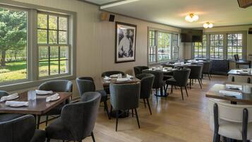 A restaurant with multiple tables and chairs, large windows, and a framed picture on the wall.