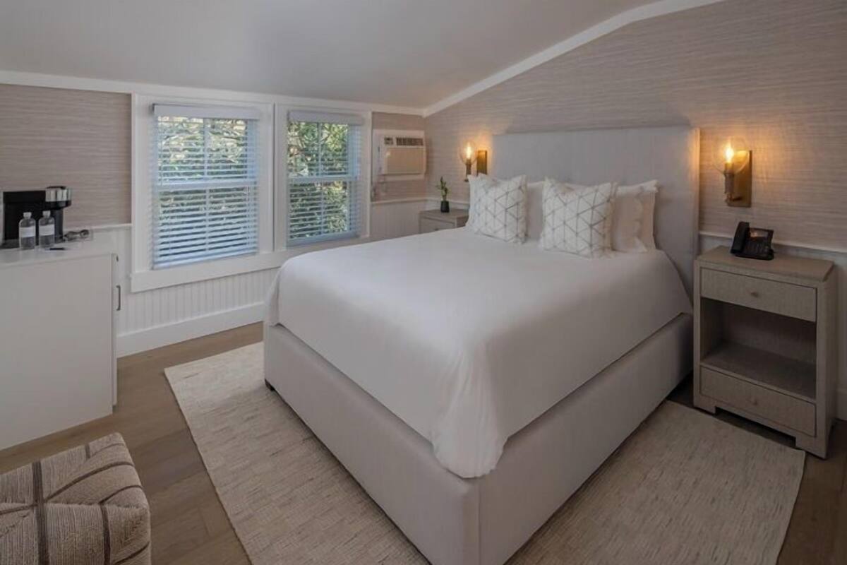 A bedroom with a large bed, bedside tables, a nightstand, a desk, and a window with blinds.