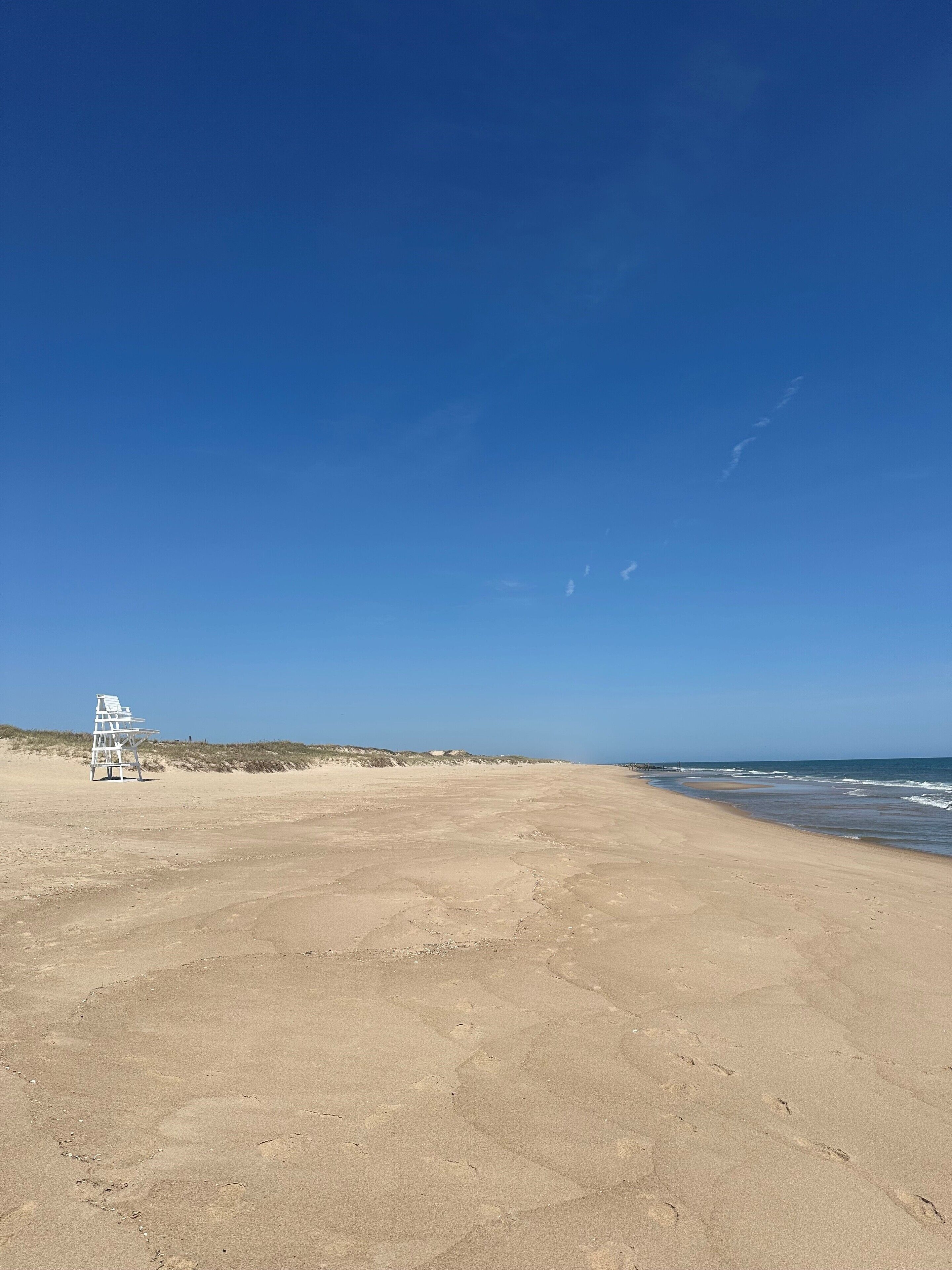 Una playa arenosa con una torre de salvavidas y un cielo azul despejado.