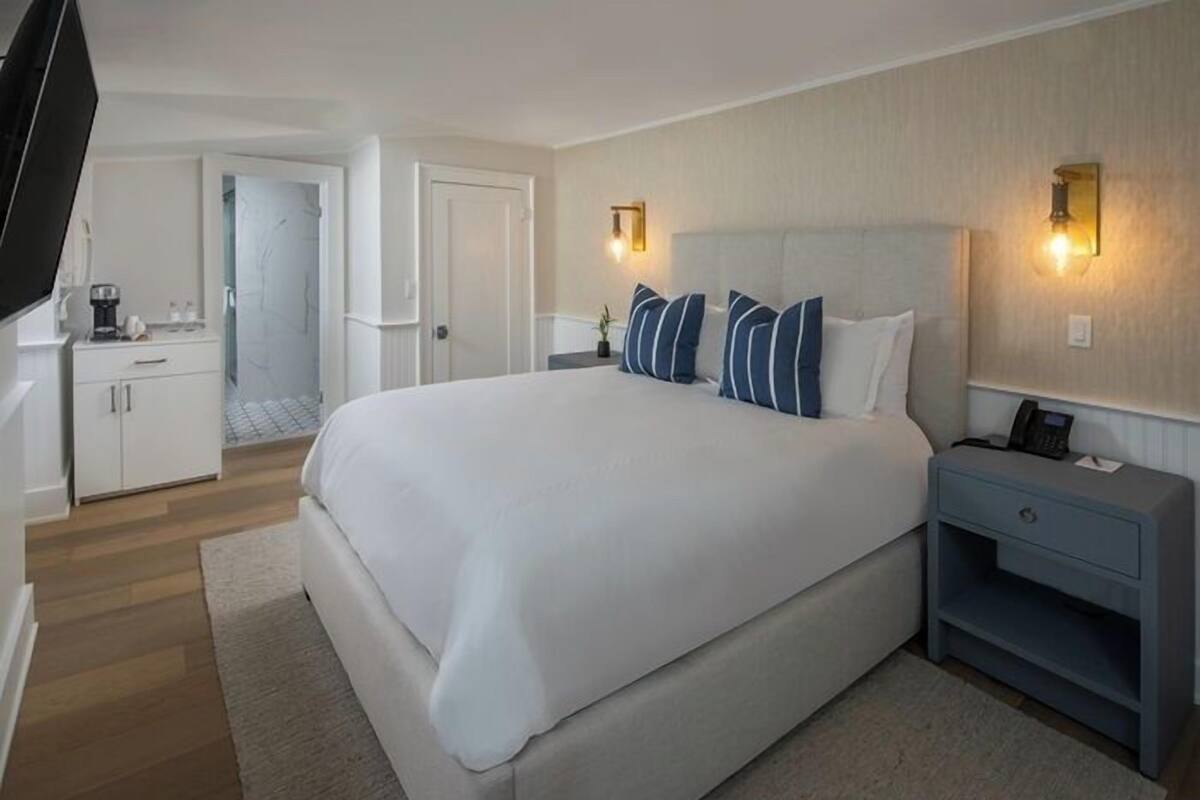 A hotel room with a large bed, bedside tables, a TV, and a bathroom visible in the background.