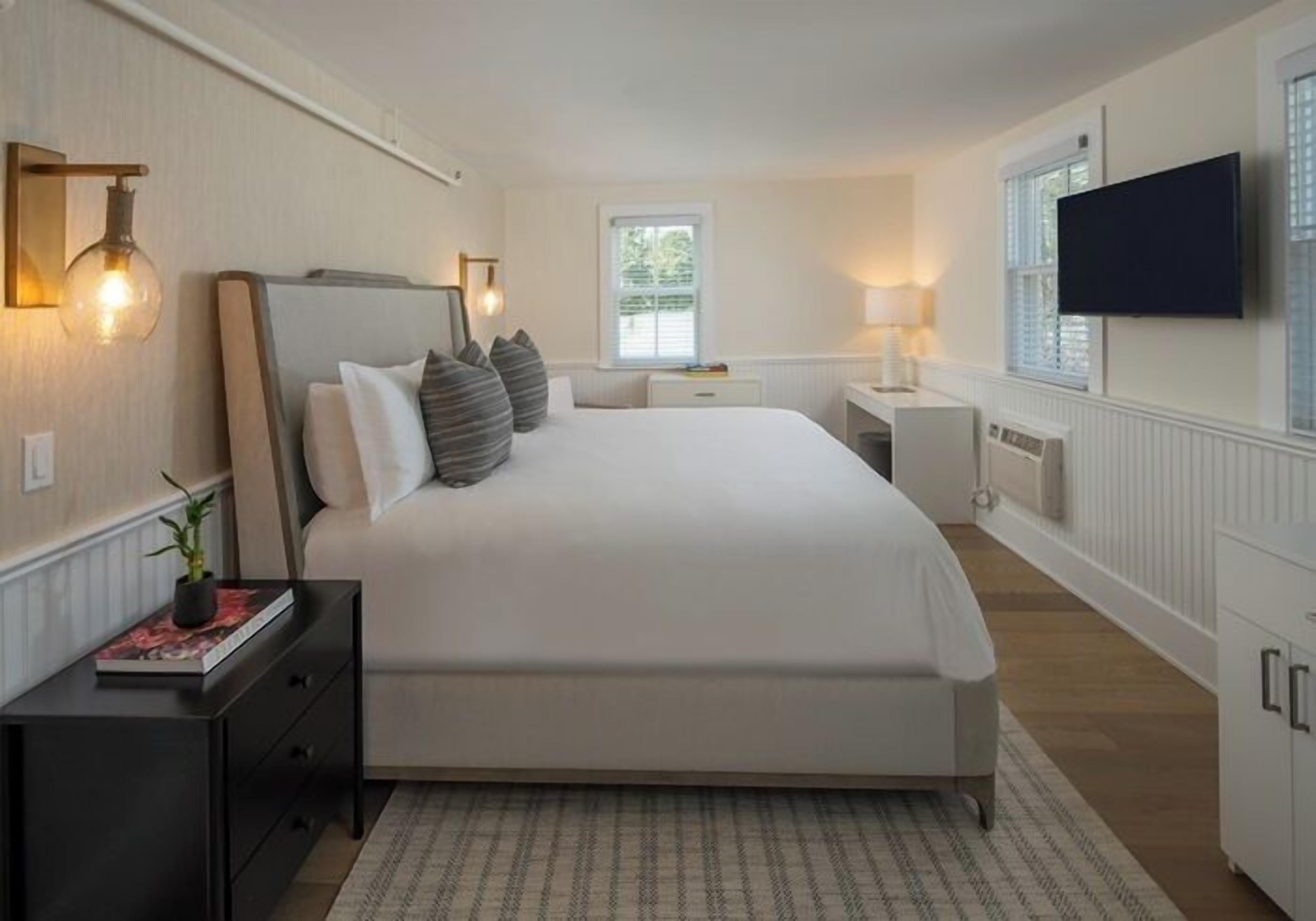 Une chambre avec un grand lit, des tables de chevet, une télévision et une fenêtre avec des stores.