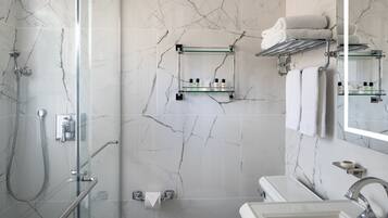 A modern bathroom with a glass shower enclosure, a glass shelf with toiletries, and a large mirror.
