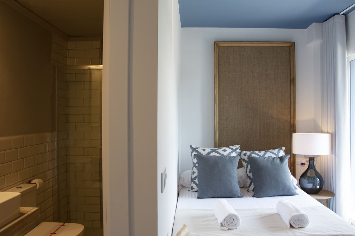 Une chambre d’hôtel avec une douche, un lit avec deux oreillers, une table de chevet avec une lampe et une fenêtre avec des rideaux.