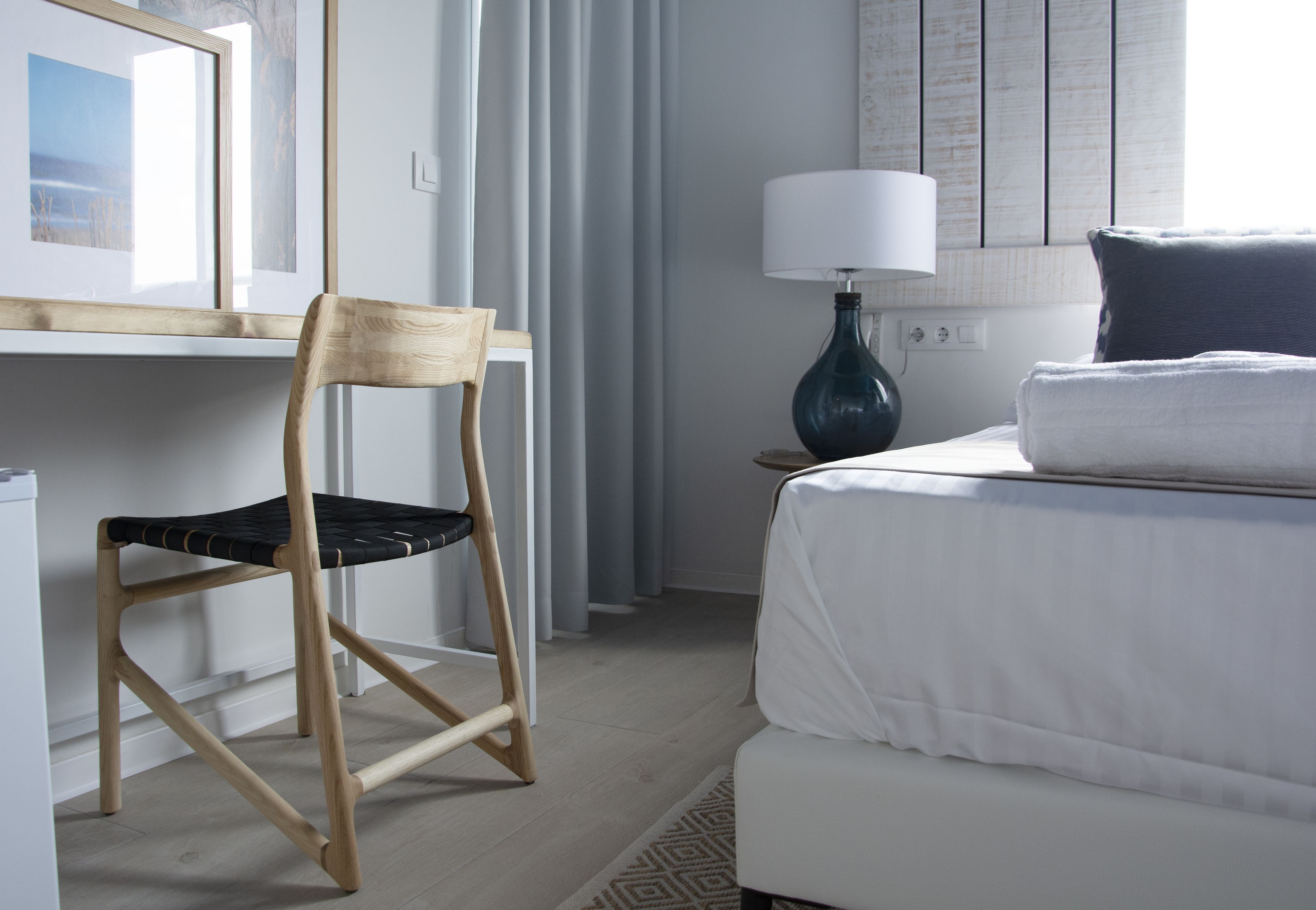 Una habitación de hotel con cama, una silla, una lámpara y una ventana con cortinas.