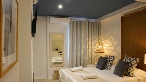Ein modernes Hotelzimmer mit einem großen Bett, einem Nachttisch, einem kleinen Hocker und einem Spiegel.