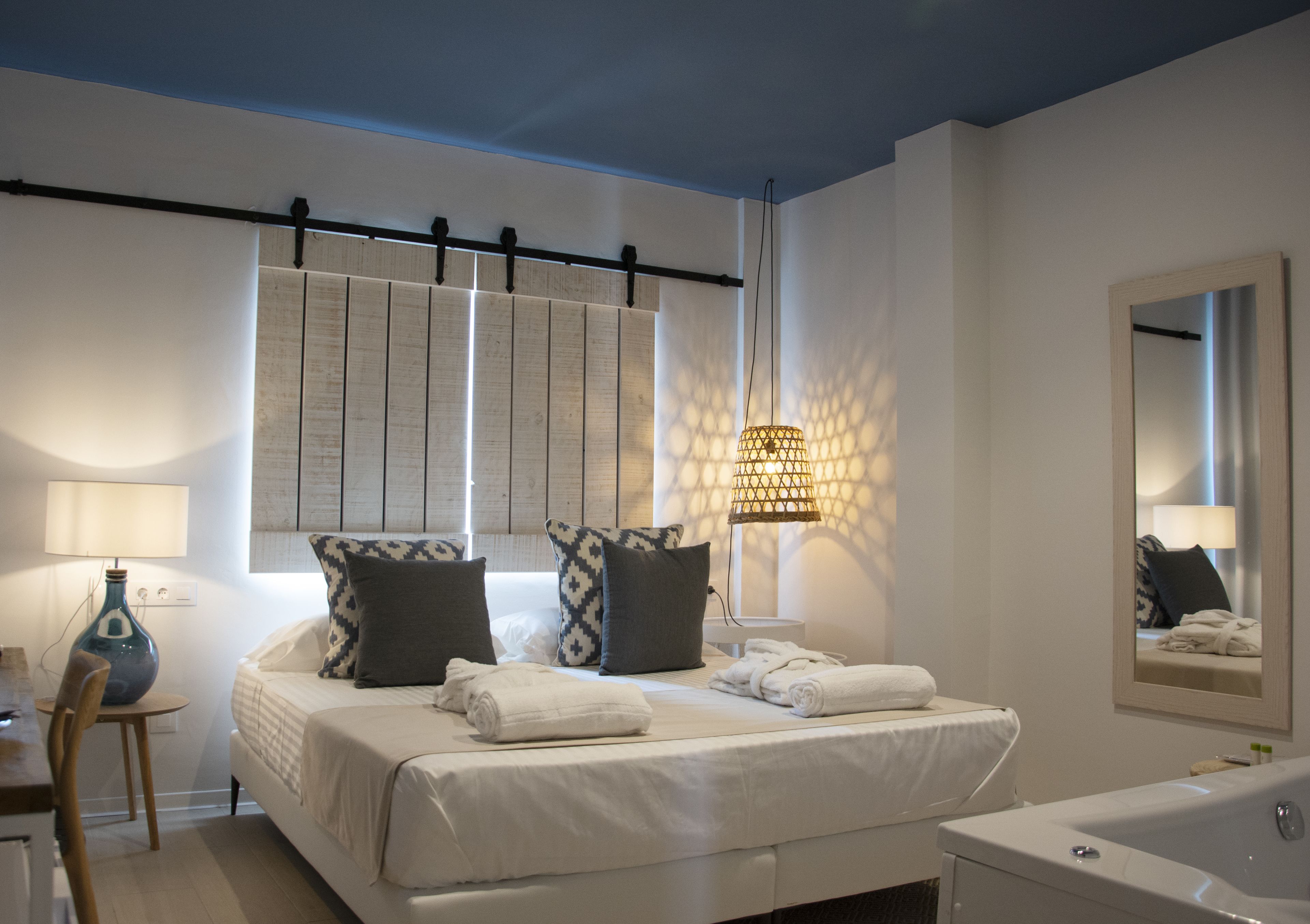 A bedroom with a bed, bedside lamps, a mirror, and a bathroom with a bathtub.
