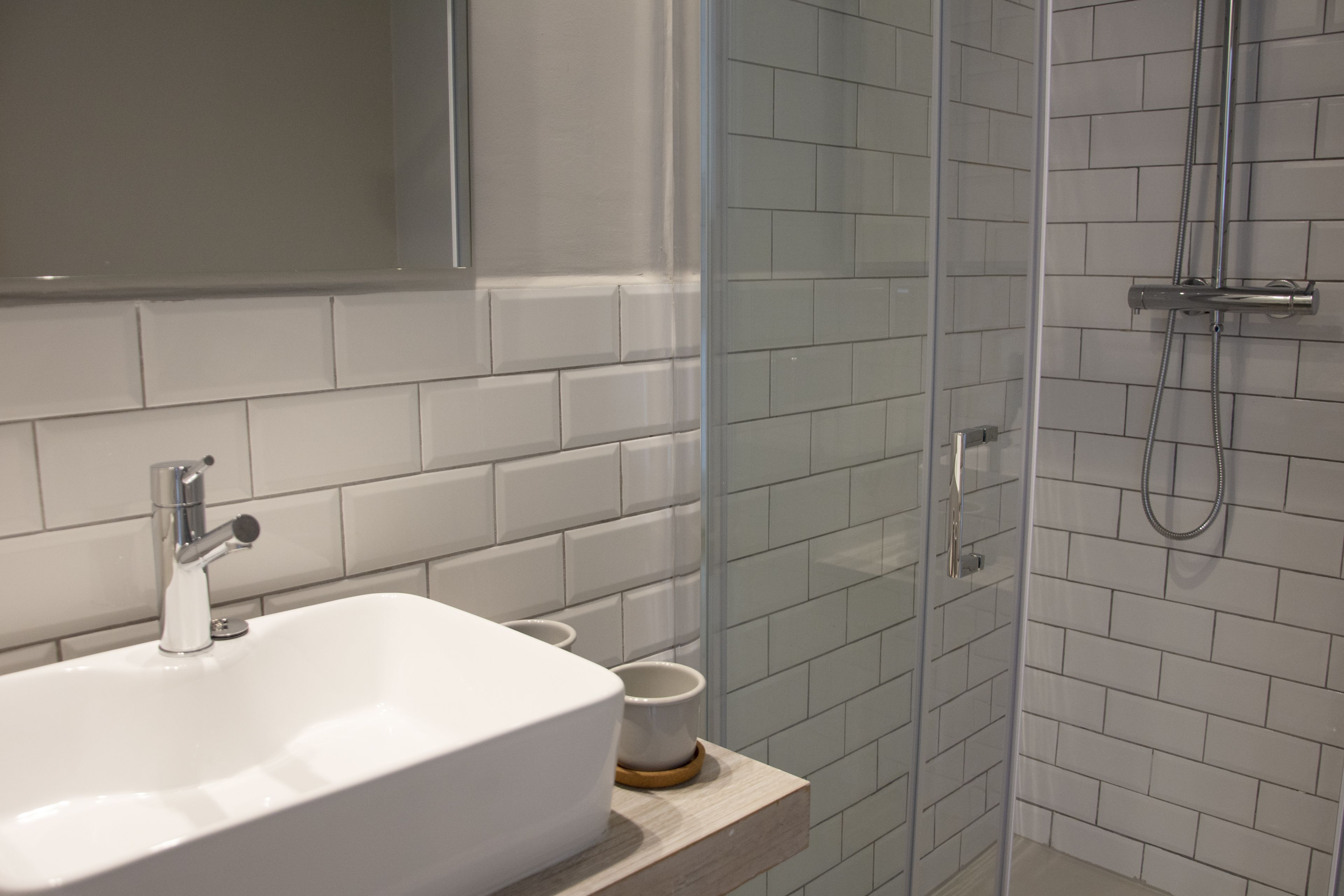 Un baño con un lavamanos blanco, cabina de ducha con vidrio y paredes cubiertas de azulejos blancos.