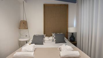 Una habitación de hotel con una cama, dos almohadas, una mesita de noche con una lámpara y una ventana con cortinas.
