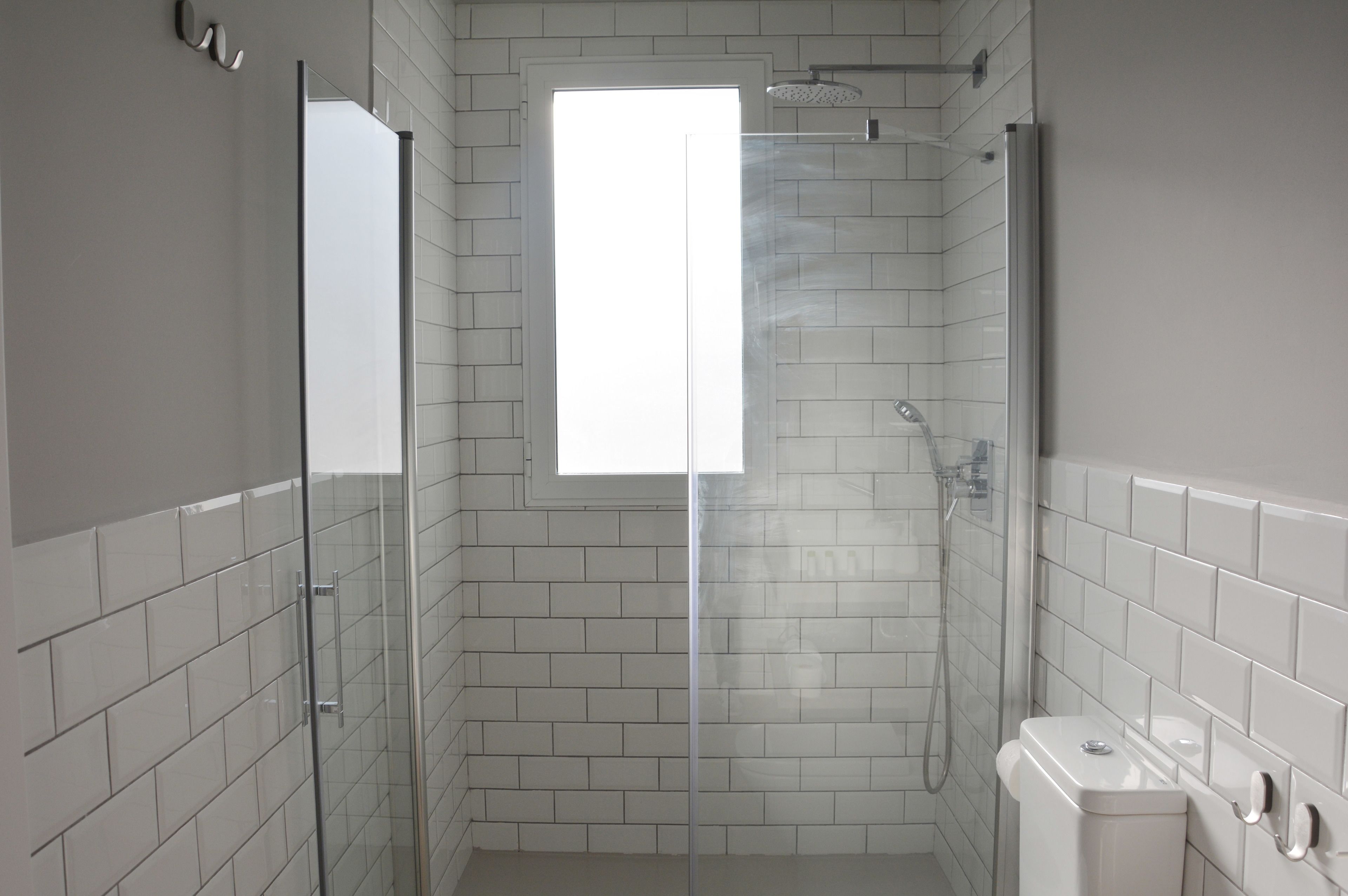 Un baño moderno con paredes de azulejos blancos, cabina de ducha de vidrio, inodoro y lavabo.