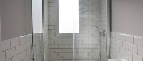 Un baño moderno con paredes de azulejos blancos, cabina de ducha de vidrio, inodoro y lavabo.