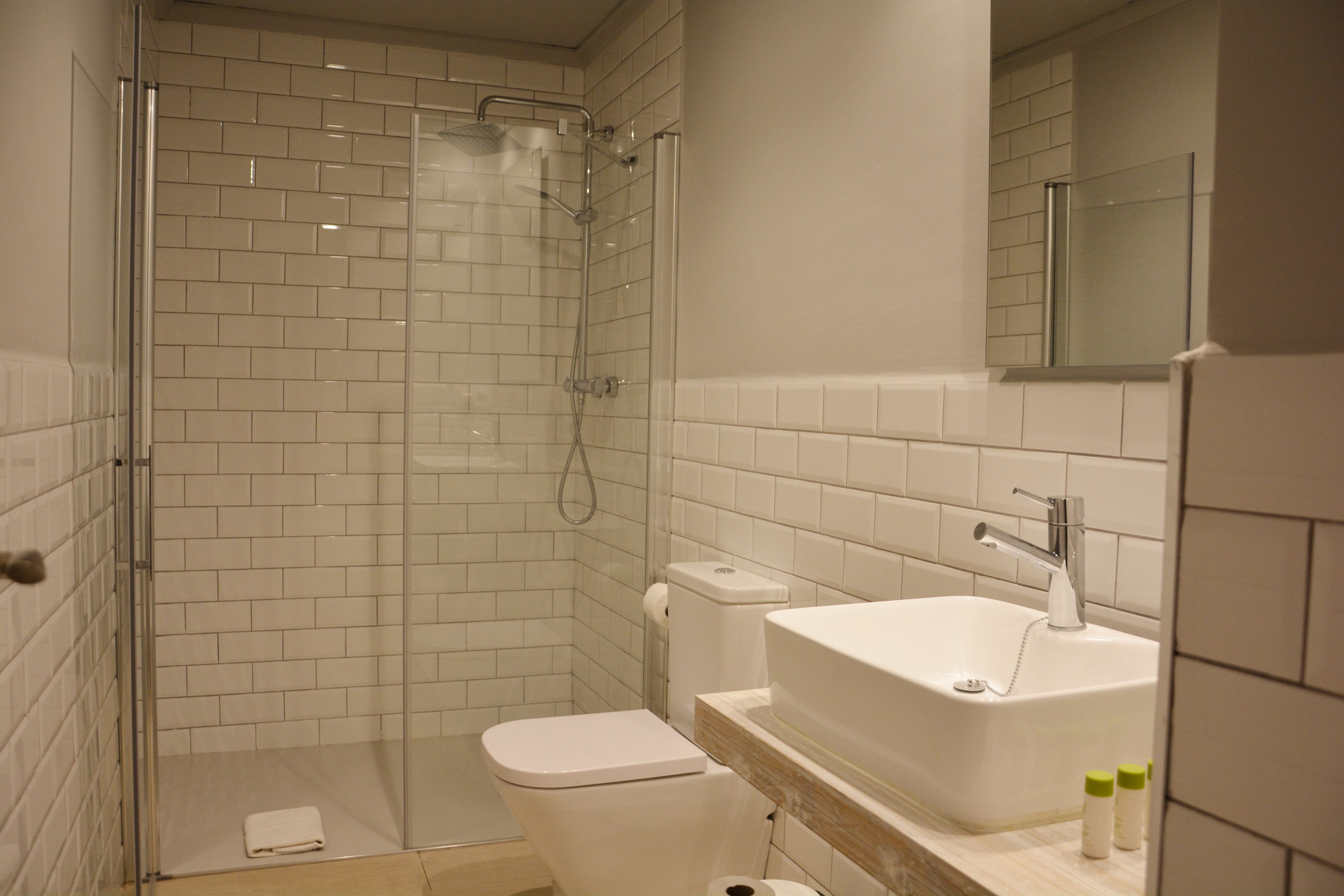 Un baño con ducha de vidrio, inodoro blanco y lavamanos con espejo.