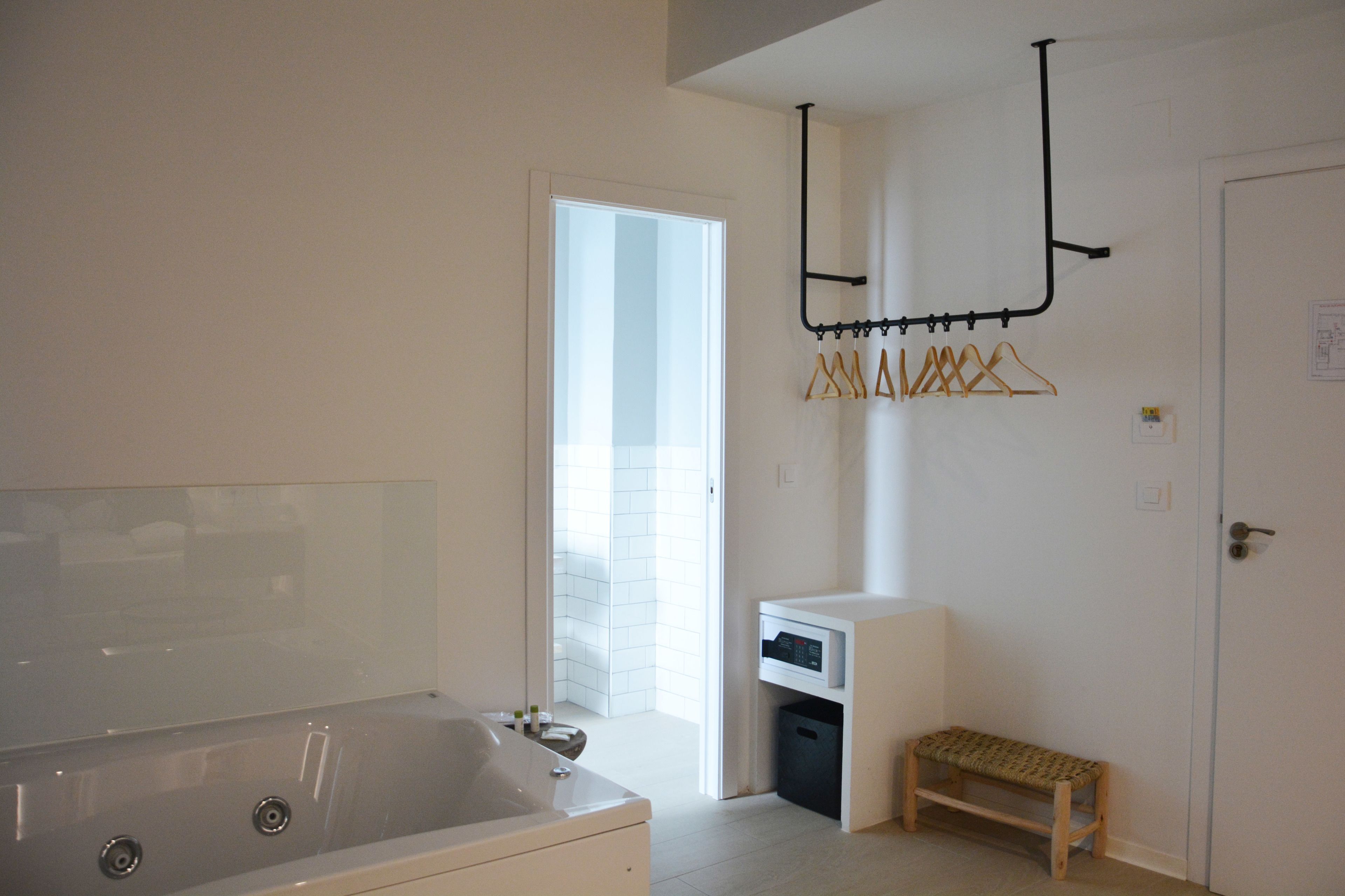 A modern bathroom with a large bathtub, a small bench, and a drying rack with clothes.