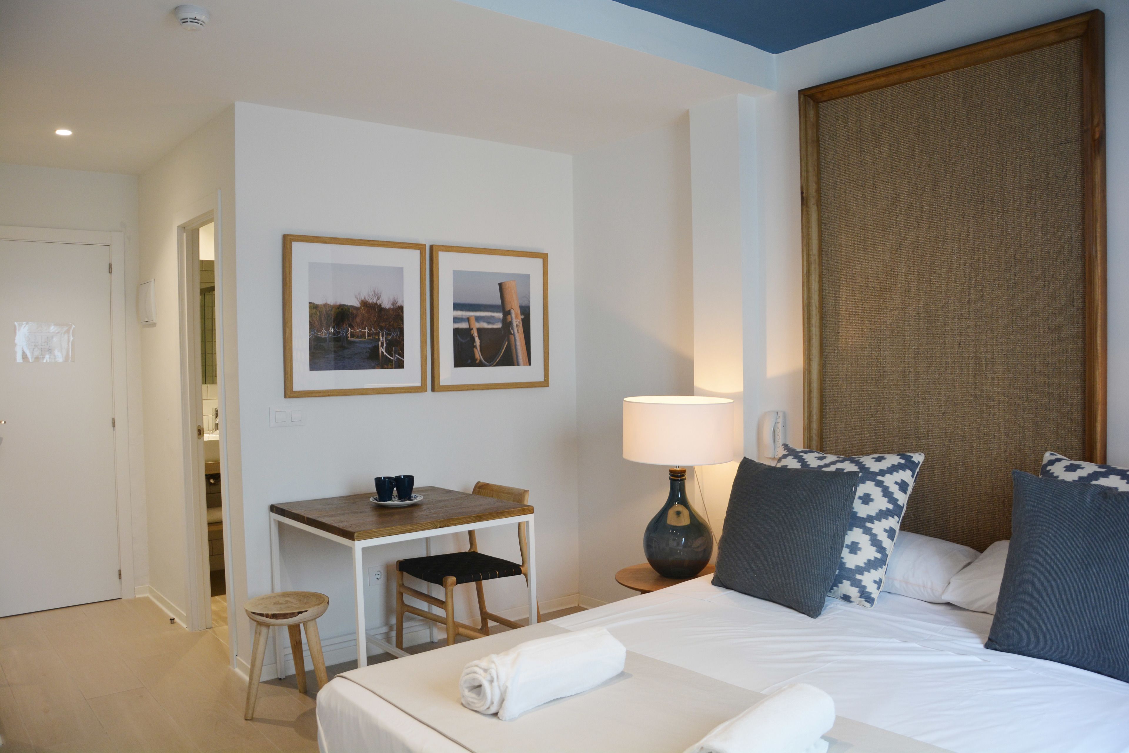 Ein Hotelzimmer mit einem Bett, einem Schreibtisch, einem Sessel, einer Lampe und zwei gerahmten Bildern an der Wand.