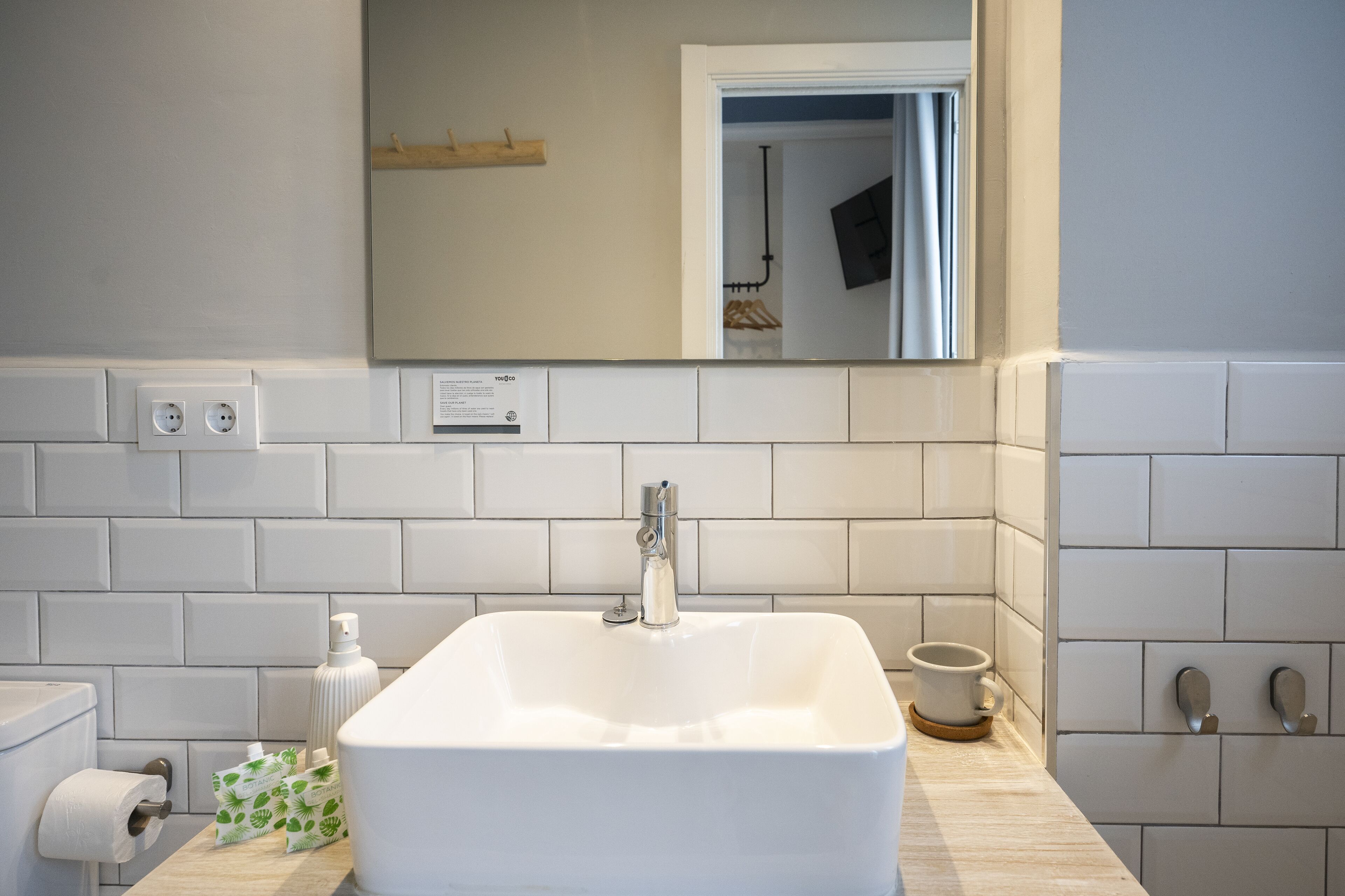 A bathroom with a white sink, a mirror, a toilet, and a towel dispenser.