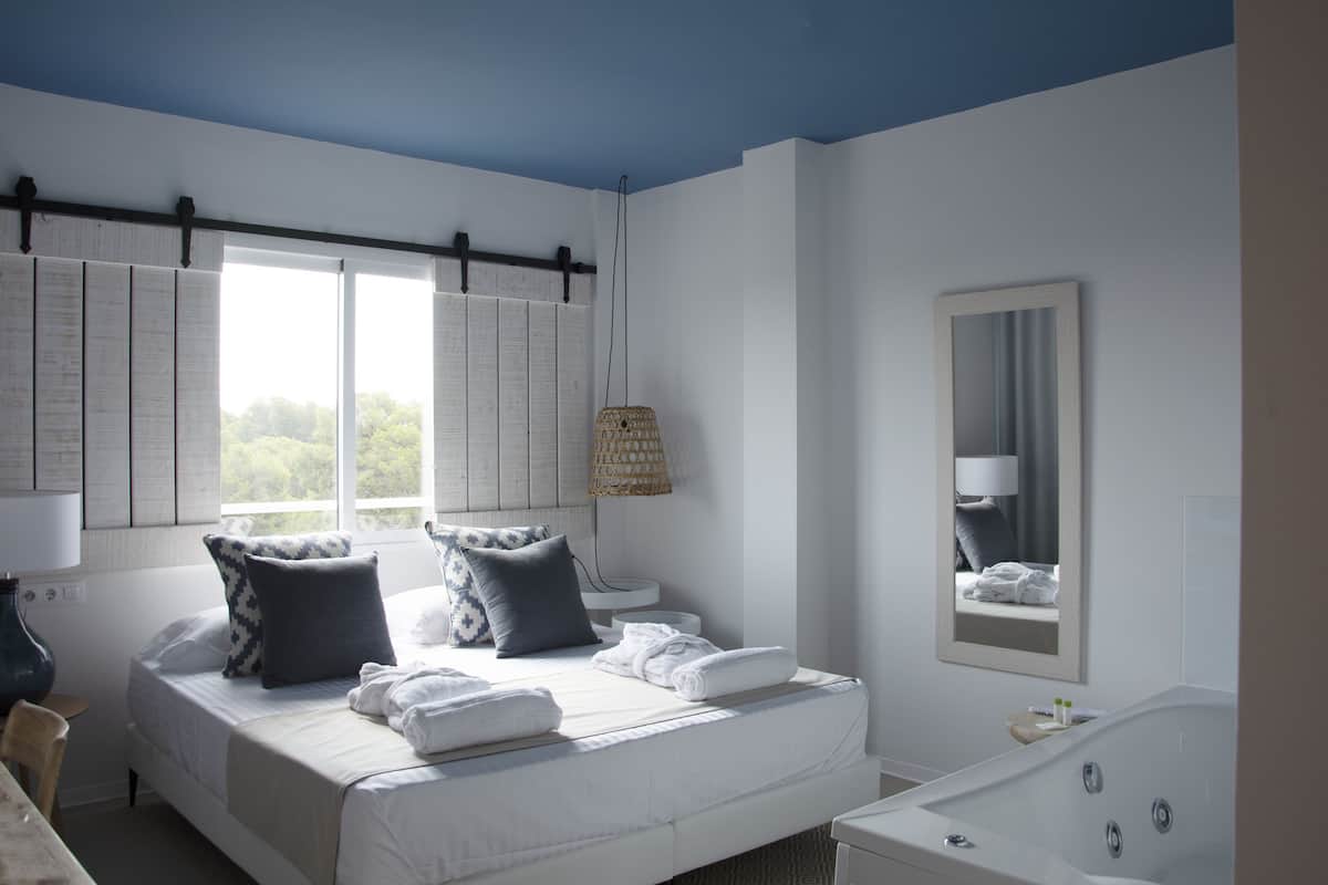 Une chambre à coucher comprenant un lit, une table de chevet, une lampe, une fenêtre et une salle de bain avec une baignoire.