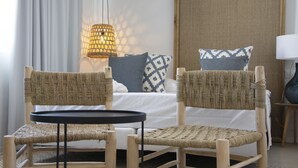 Ein Zimmer mit einem Bett, zwei Korbstühlen, einem kleinen Tisch, einer Lampe und einer Wandleuchte.