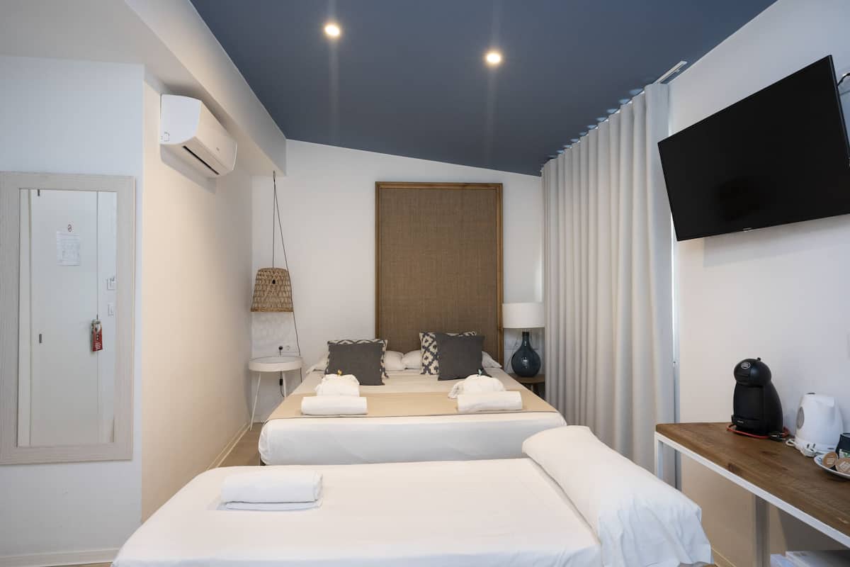 Une chambre d’hôtel avec deux lits, un téléviseur à écran plat, un climatiseur, une table de chevet avec une machine à café et une fenêtre avec des rideaux.