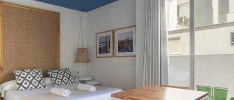 A bedroom with a bed, bedside tables, a wooden table, and a large window.