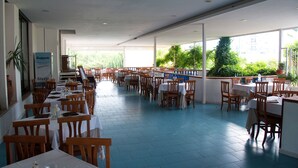 A spacious restaurant with multiple tables and chairs, large windows, and indoor plants. - La Sorgente (Capaccio-Paestum)