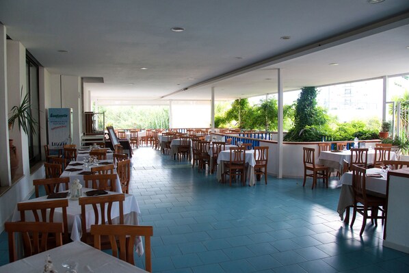 A spacious restaurant with multiple tables and chairs, large windows, and indoor plants. - La Sorgente (Capaccio-Paestum)