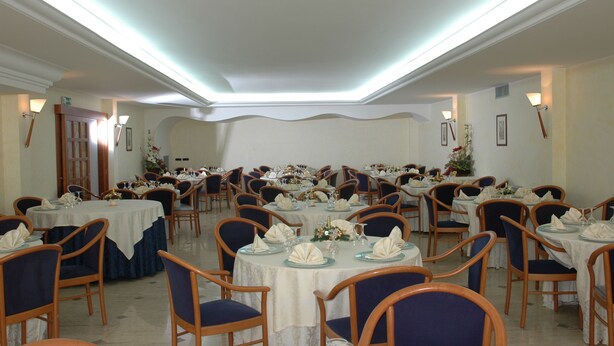 Un salón de banquetes con mesas redondas, sillas y un techo alto con iluminación empotrada.